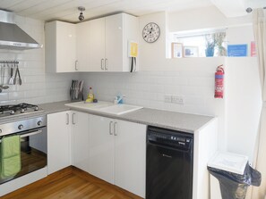 Une cuisine avec des meubles blancs, une cuisinière, un lave-vaisselle et une horloge au mur.