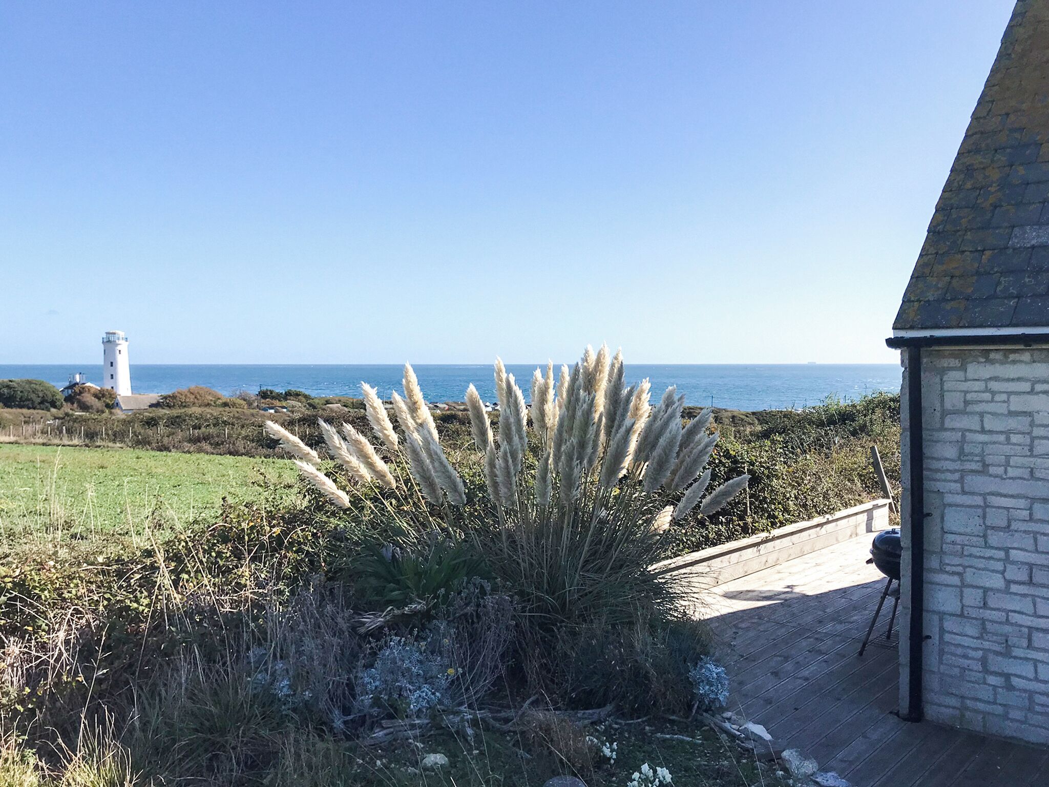 A coastal view with a lighthouse, a grassy field, and a building with a stone facade.