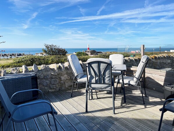 Une terrasse avec des sièges extérieurs, une vue sur la mer et un phare visible au loin.