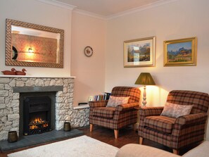 A cozy living room with a stone fireplace, two plaid armchairs, a bookshelf, and framed artwork on the walls. - Catbells Cottage (Keswick) (Keswick)