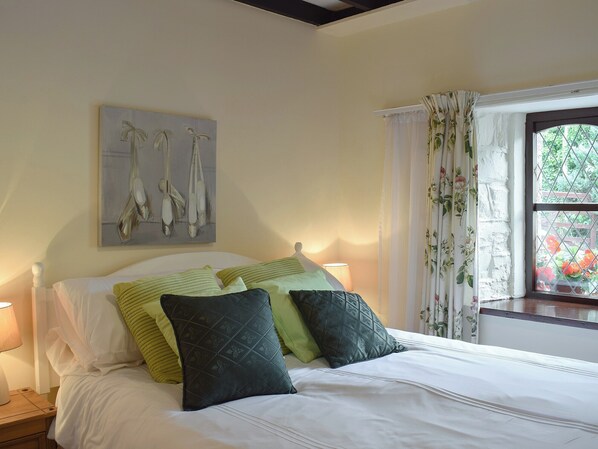 A neatly made bed with white linens and green pillows, a painting of birds on the wall, and a window with floral curtains. - 3 bedroom accommodation in New Quay (New Quay)