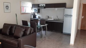 A compact living space with a sofa, dining table, chairs, a kitchen area including a microwave, coffee maker, and a refrigerator. - Complejo los Guindos - Ushuaia Flat (Ushuaia)