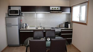 A compact kitchen with a refrigerator, microwave, stove, and a dining area with two chairs. - Complejo los Guindos - Ushuaia Flat (Ushuaia)
