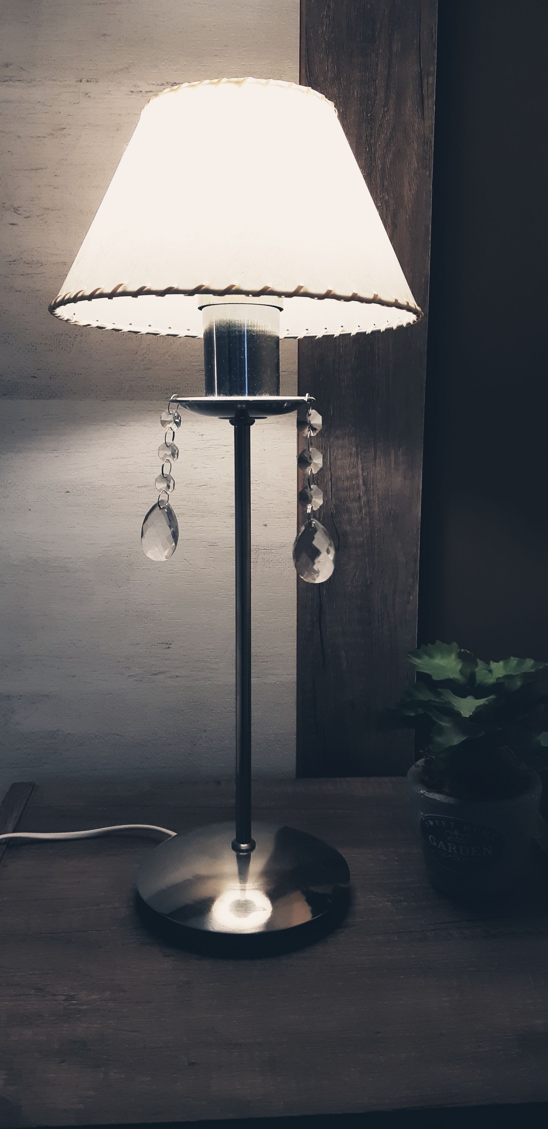 En bordslampa med en vit lampskärm och kristalldekorationer, placerad på ett träbord.