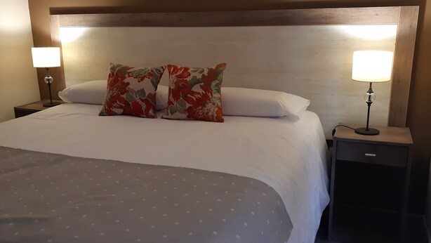 A neatly made bed with a floral pillow, two bedside lamps, and a wooden headboard. - Complejo los Guindos - Ushuaia Flat (Ushuaia)