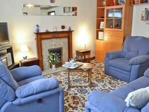 A living room with two blue armchairs, a fireplace, a small table with a tray of items, and a bookshelf.
