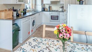 Ett modernt kök med vita skåp, en tvättmaskin, en ugn och en matplats med ett blommigt bordsduk.