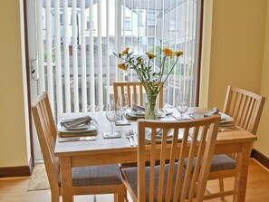 A dining table set for four with chairs, a vase with flowers, and a view of buildings through the window.