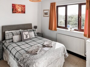 Quarto com cama, mesa de cabeceira, janela com cortinas, radiador e um quadro na parede.