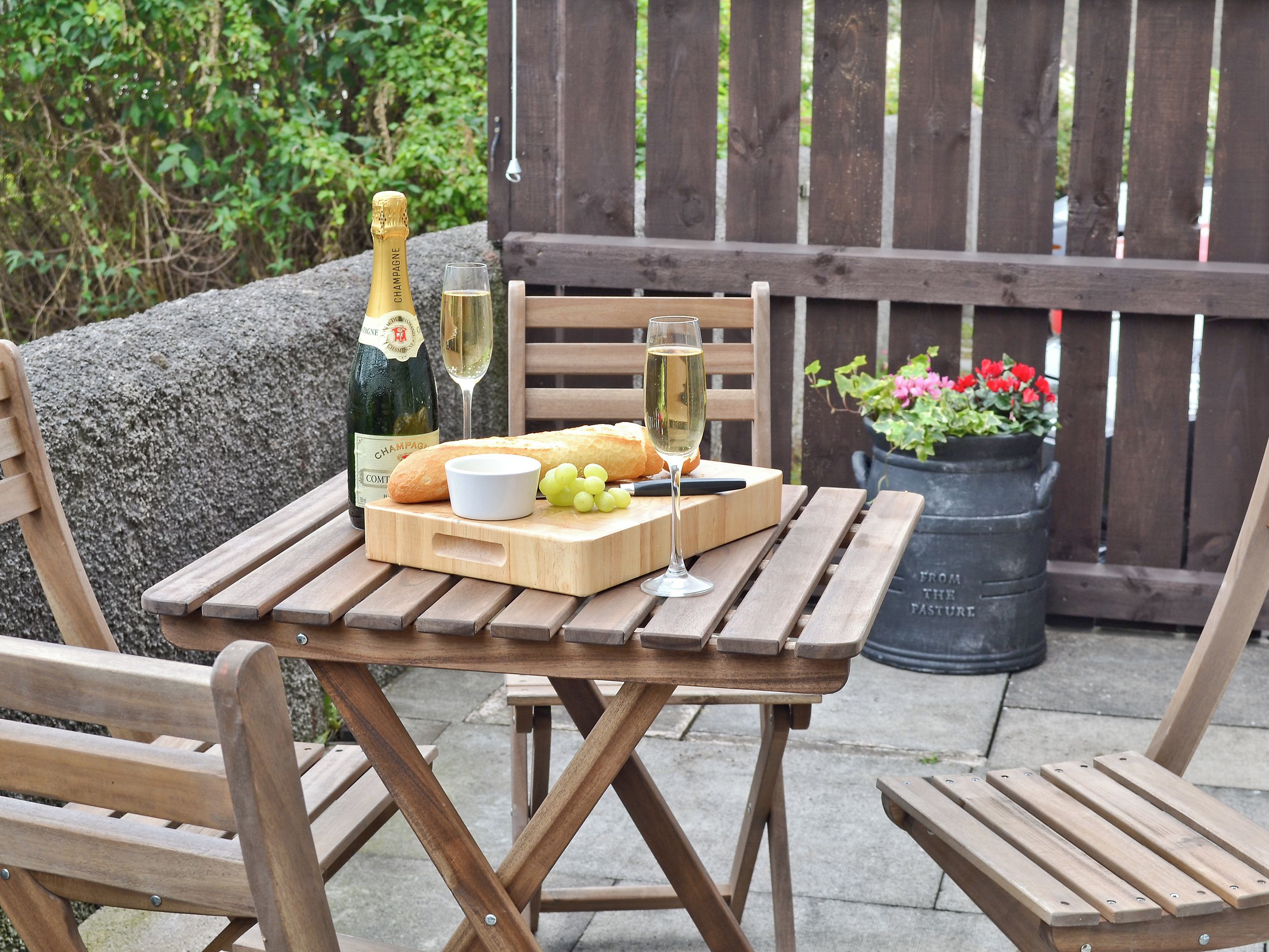 Ein Holztisch mit einer Champagnerflasche, einem Glas, einem Baguette und einer kleinen Schüssel mit Trauben.
