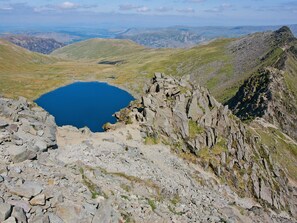 A rugged mountain landscape with a clear blue lake surrounded by rocky terrain and distant hills.