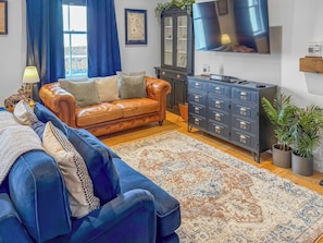 A living room with a leather sofa, a blue sofa, a patterned rug, a cabinet, and a TV.