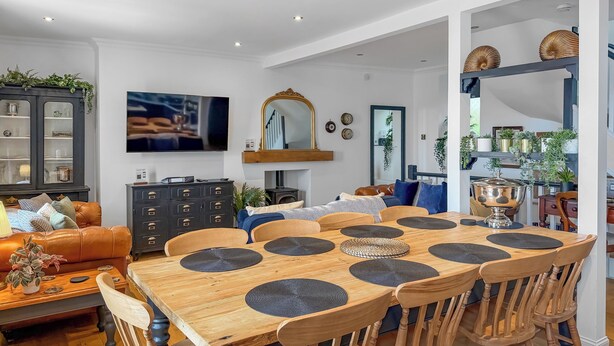 Un comedor con una mesa de madera, sillas y un televisor al fondo.