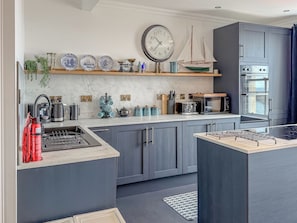 A modern kitchen with grey cabinets, a central island, a clock, and a stove.