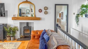 Una sala de estar con un sofá de cuero marrón, una chimenea, un espejo y una escalera.