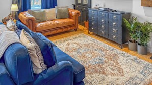 Un salón con un sofá de cuero, un sofá azul, un tapete estampado, un aparador y un televisor.