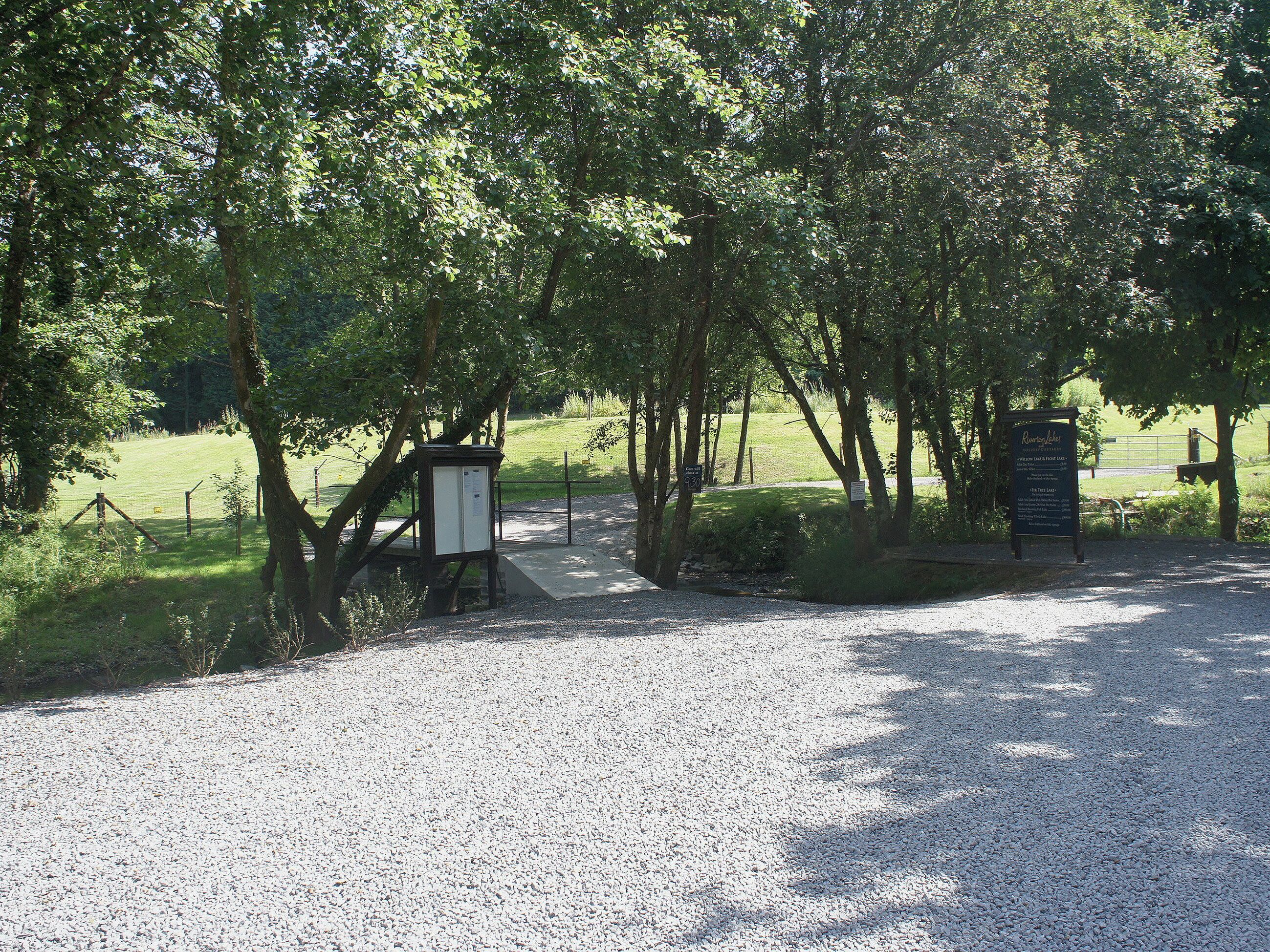 Un sendero de grava que conduce a un parque con árboles y un cartel.
