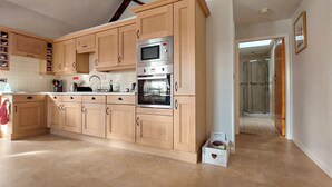 A modern kitchen with wooden cabinets, stainless steel appliances, and a tiled floor. - 1 bedroom accommodation in Wansford, near Driffield (Wansford, near Driffield)