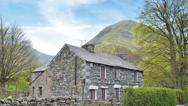 A stone house with a sloped roof, a wooden fence, and a mountain in the background. - Brothersfield Cottage (Hartsop, near Patterdale)