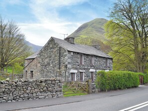 A stone house with a sloped roof, a wooden fence, and a mountain in the background. - Brothersfield Cottage (Hartsop, near Patterdale)
