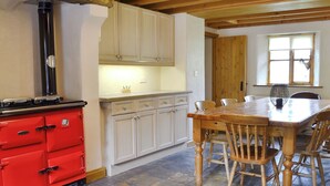 A kitchen with a red stove, white cabinets, a wooden dining table with chairs, and a window with a view. - Brothersfield Cottage (Hartsop, near Patterdale)