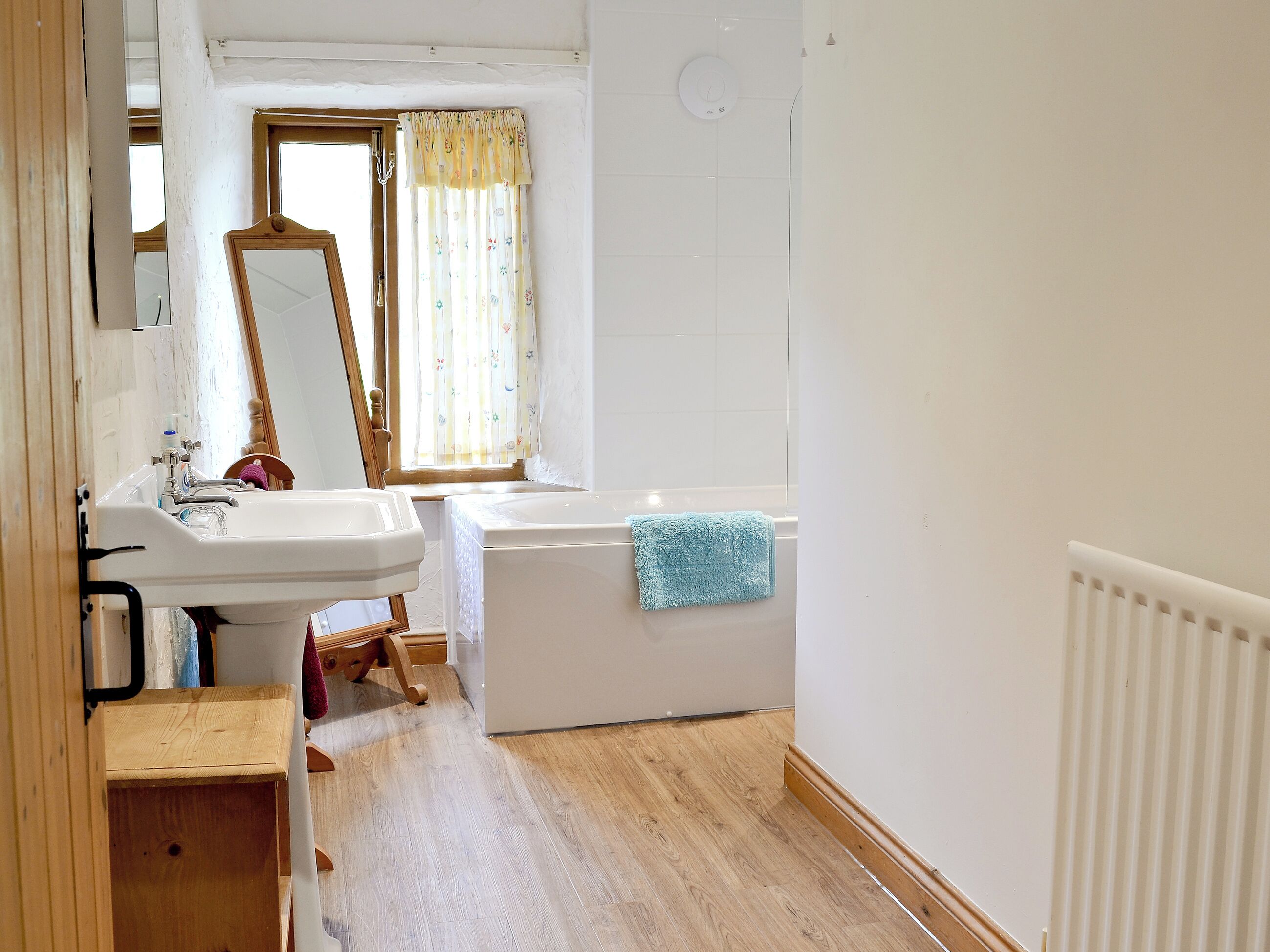 A bathroom with a sink, mirror, window with curtains, and a bathtub.