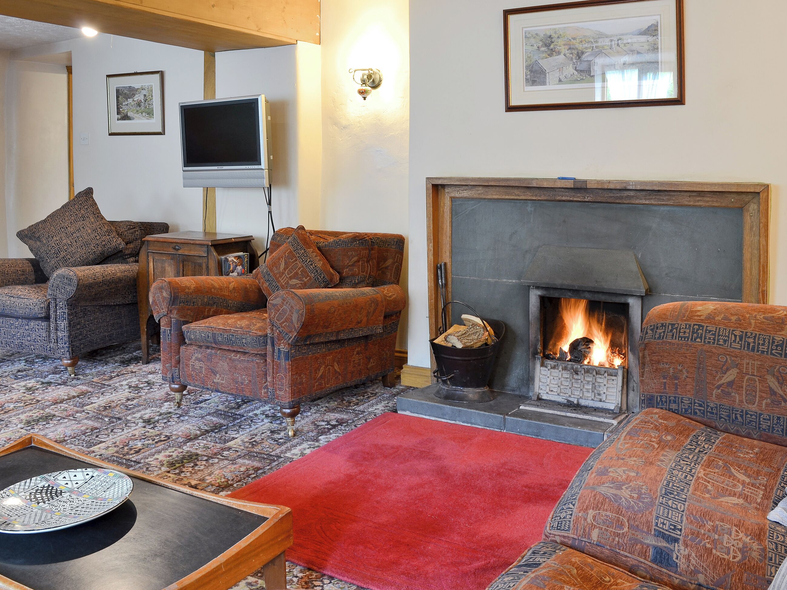 Una sala de estar con sofás estampados, una chimenea, un televisor y una alfombra roja.