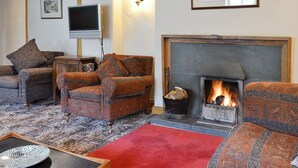 A living room with patterned sofas, a fireplace, a television, and a red rug. - Brothersfield Cottage (Hartsop, near Patterdale)