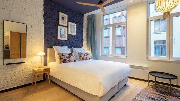 Un dormitorio moderno con una cama grande, un ventilador de techo y una ventana con cortinas.