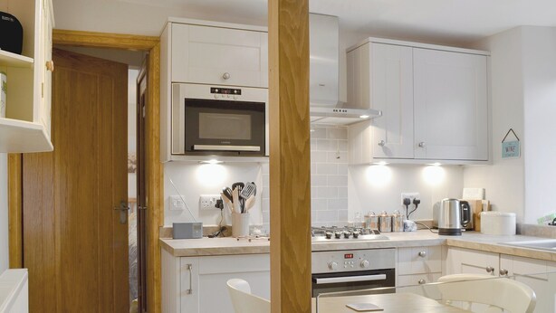 A compact kitchen with white cabinets, a microwave, a stove, and a dining area with a table and chairs. - 1 bedroom accommodation in Ambleside (Ambleside)