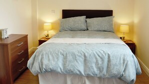 Un lit bien fait, avec une tête de lit, deux lampes de chevet et une commode en bois dotée de tiroirs.