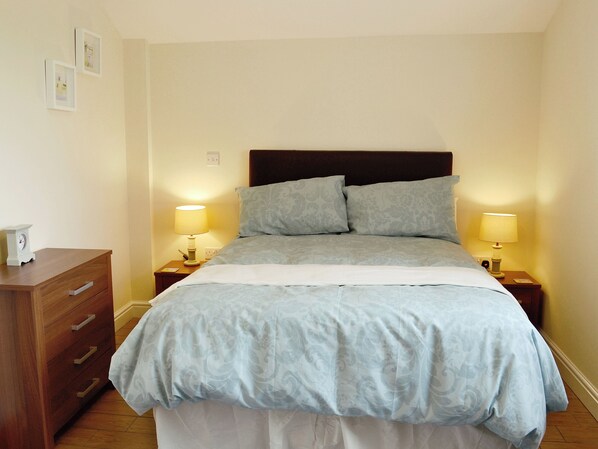 A neatly made bed with a headboard, two bedside lamps, and a wooden dresser with drawers. - 1 bedroom accommodation in Skegness (Skegness)