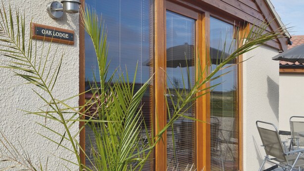 Une fenêtre à cadre en bois, sur laquelle on peut lire l’inscription « Oak Lodge », et un espace patio aménagé avec des chaises et une table.