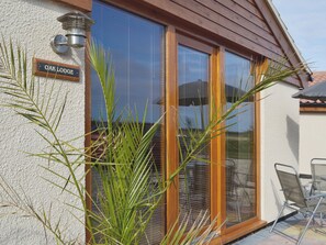 A wooden-framed window with a sign reading "Oak Lodge" and a patio area with chairs and a table. - 1 bedroom accommodation in Skegness (Skegness)