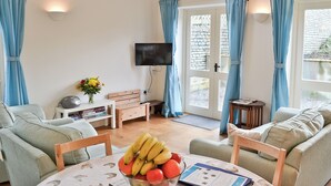 Una sala de estar con un sofá, una mesa con fruteros, un televisor y una mesita auxiliar con un florero.