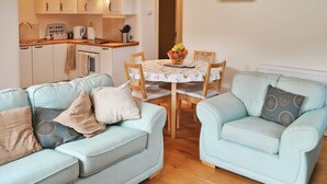 Una sala de estar con dos sofás azul claro, una mesa de comedor con sillas, y una cocina al fondo.