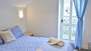 Un dormitorio con cama, almohadas, una mesita de noche y una puerta con cortinas.