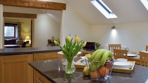 Een keuken met een eethoek, houten kasten, een vaas met bloemen en een fruitmand op het aanrecht.