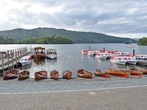 A lakeside dock with various boats, including wooden rowboats and motorboats, anchored and tied up.