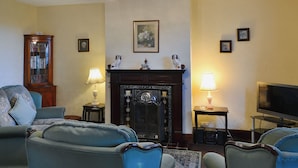 Un salon avec une cheminée, deux fauteuils, un canapé, une télévision et une bibliothèque.