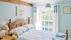 Une chambre à coucher avec un lit en bois, une table de chevet, une lampe et une fenêtre avec des rideaux.