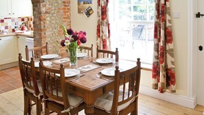 Un coin repas avec une table en bois dressée pour quatre personnes, entourée de chaises dotées d’assises rembourrées. Un vase rempli de fleurs est posé sur la table.
