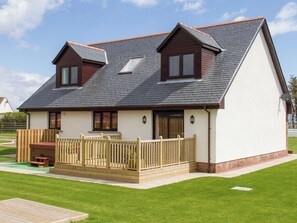 Une maison à deux étages avec un toit en pente, une terrasse en bois et une cour clôturée.