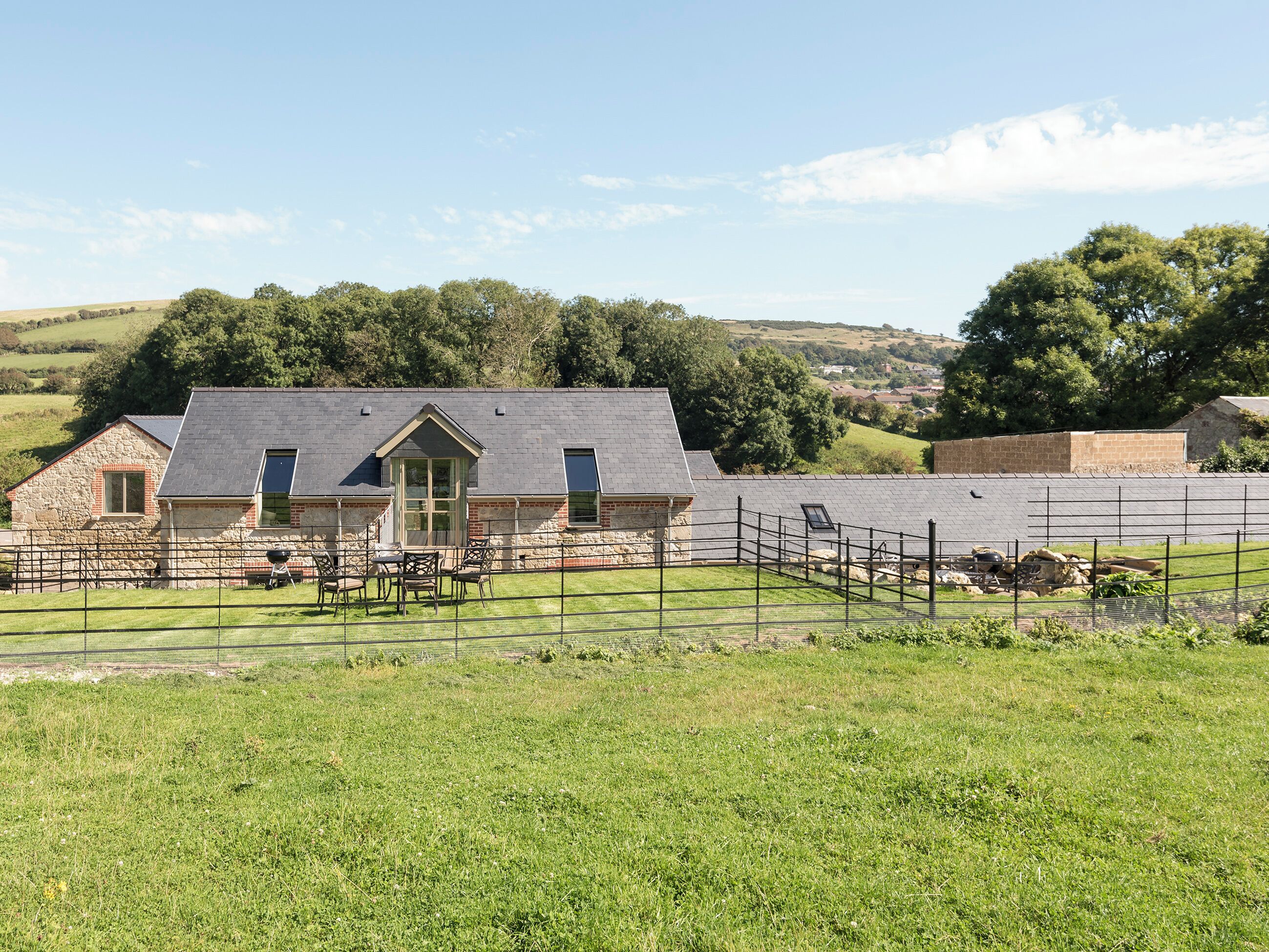A stone farmhouse with a fenced yard and a clear view of the surrounding countryside.
