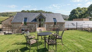 Un bâtiment en pierre avec un toit en pente, un petit porche et un espace extérieur clos, aménagé avec une table et des chaises.