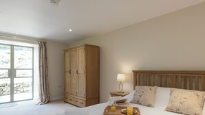 Une chambre à coucher avec un lit, une armoire en bois, une table de chevet avec une lampe et un plateau avec un verre de jus d’orange.