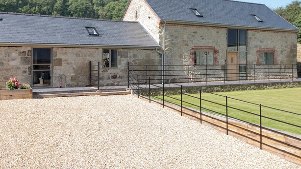 Un bâtiment en pierre avec une allée en gravier et une pelouse délimitée par une clôture.