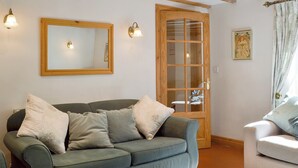 Un salon chaleureux avec un canapé vert, une porte en bois et un petit fauteuil blanc.