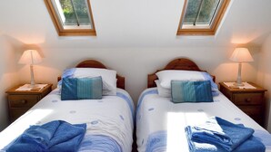 Une chambre double avec deux lits, chacun doté d’une table de chevet et d’une lampe. Des fenêtres de toit sont situées au-dessus des lits.