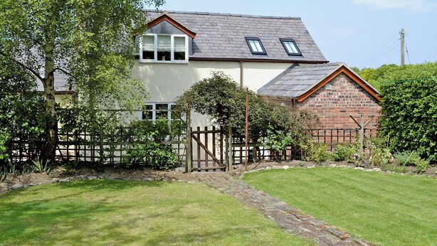 Une maison à deux étages avec une façade en briques, un toit en tuiles et un jardin clos.